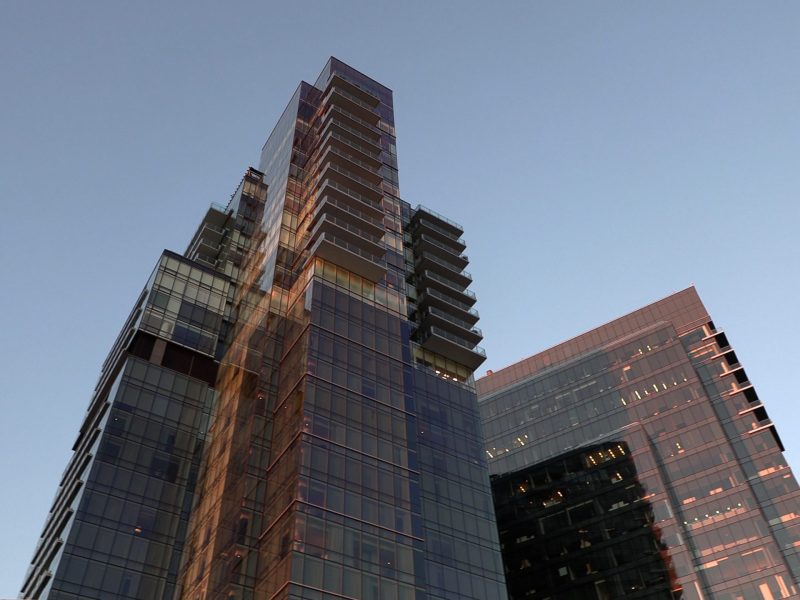 A photo of the Baltimore Four Seasons hotel taken from the ground. It is a high rise building with a glass and steel facade, set against a clear blue sky.