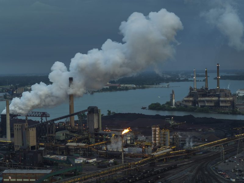 Photo of industrial site on a river, with smoke rising from smokestacks