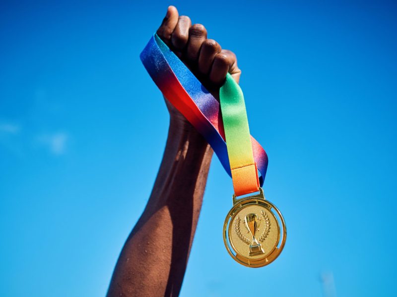 Raised hand holding a gold medal against blue sky. Photo via Getty Images