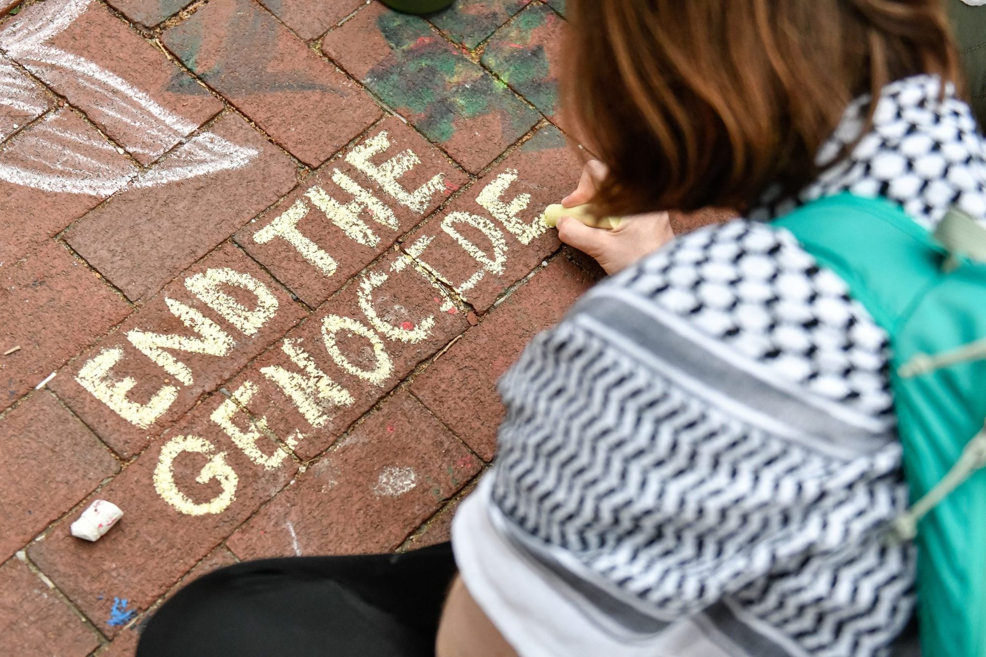 A protestor writes pro-Palestinian slogans with chalk on the ground as Pro-Palestinian protestors continue protesting at the pro-Palestine encampment of the University of Michigan. Photo by Adam J. Dewey/Anadolu via Getty Images