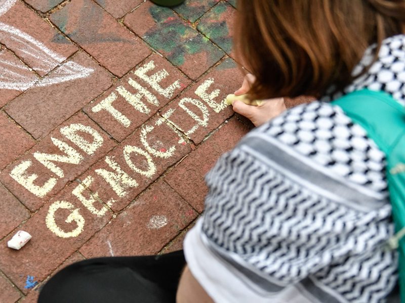 A protestor writes pro-Palestinian slogans with chalk on the ground as Pro-Palestinian protestors continue protesting at the pro-Palestine encampment of the University of Michigan. Photo by Adam J. Dewey/Anadolu via Getty Images