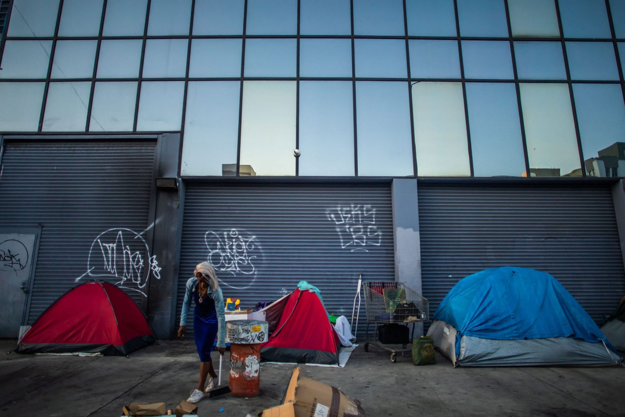 A woman sweepes a sidewalk in an encampment in Skid Row, downtown Los Angeles, California, on July 26, 2024. Photo by APU GOMES/AFP via Getty Images