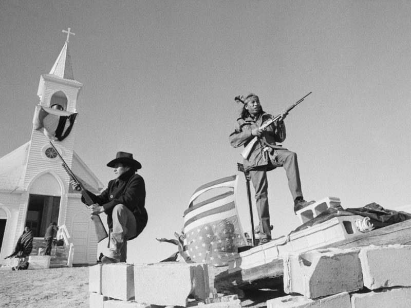 Members of the American Indian Movement and local Oglala Sioux stand guard outside the Sacred Heart Catholic Church after taking control of the town and eleven hostages during a 71 day standoff with the FBI and US Marshals.