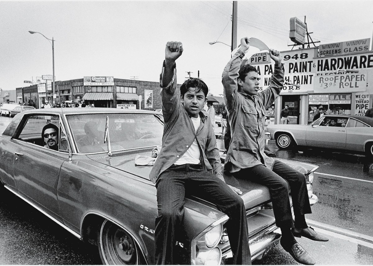 Two young Chicano men ride on the hood of a car and raise their fist during a National Chicano Moratorium Committee march in opposition to the war in Vietnam, Los Angeles, California, February 28, 1970. Photo by David Fenton/Getty Images