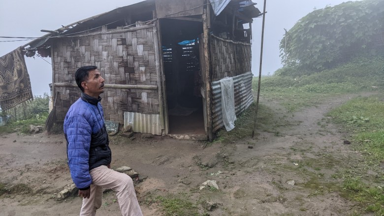 Unnamed tour guide stands outside of a shack on a foggy morning at Rungneet Tea Garden (also known as Kanchan View) in Darjeeling, India, in October 2022