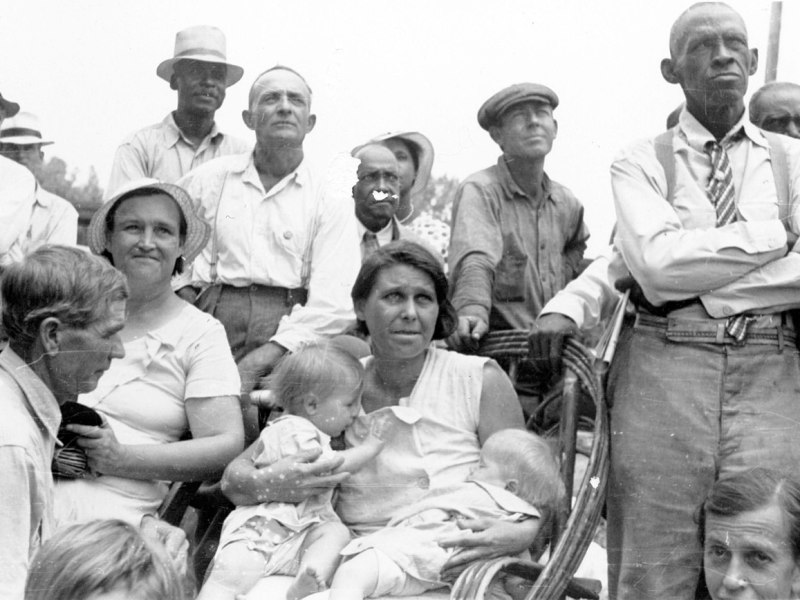 Men, women, and children, black and white, listen to a speaker at an outdoor Southern Tenant Farmers Union meeting, 1937. Wikimedia Commons