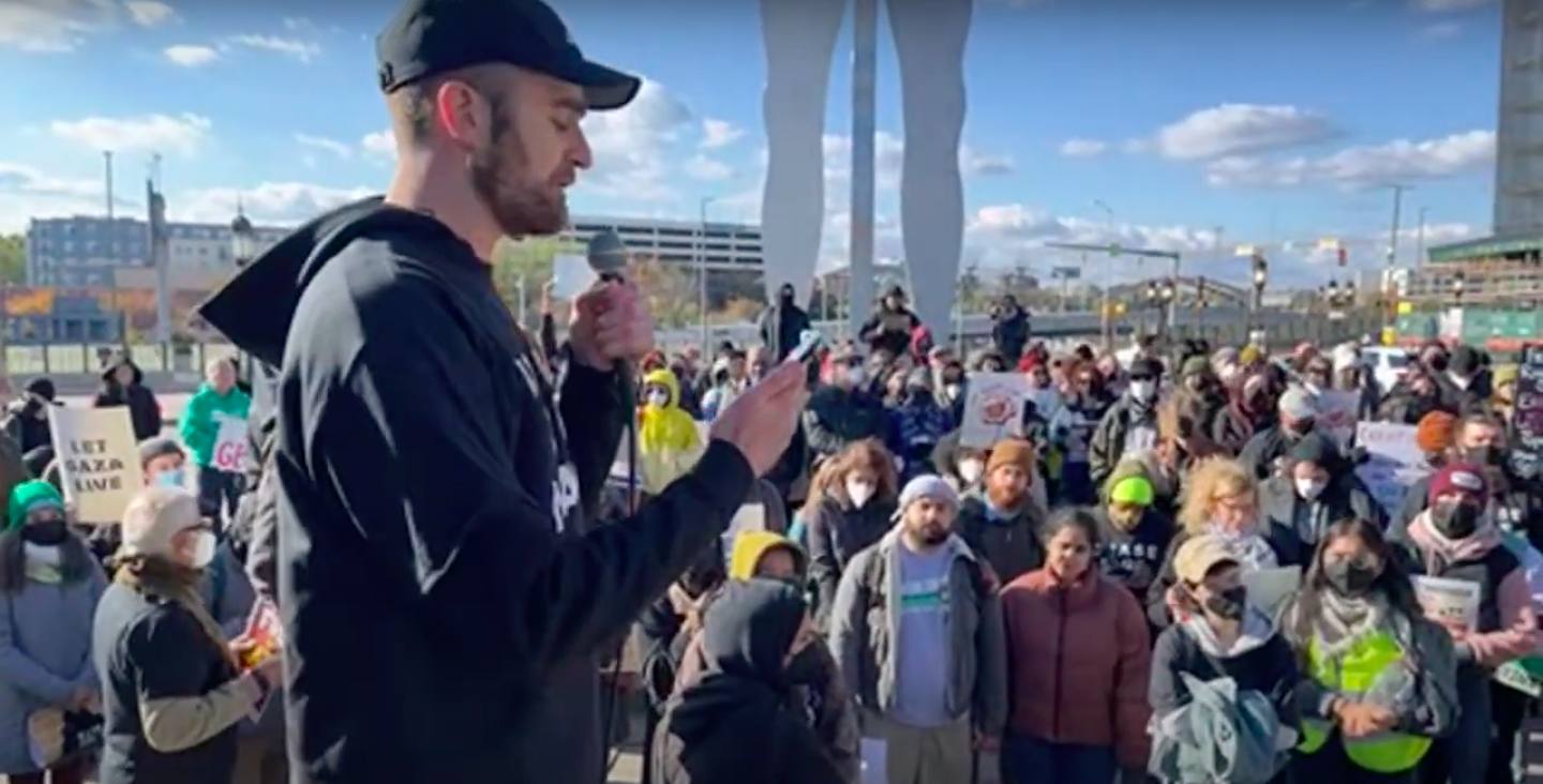 An activist speaks into a mic in front of a large crowd of people.